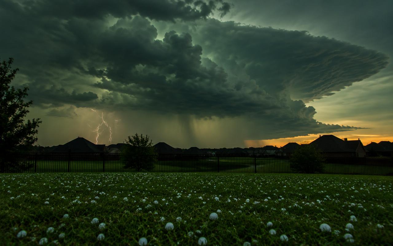 AI illustration: a dark green spring storm cloud over North Texas rooftops at dusk, with white hailstones on a lawn